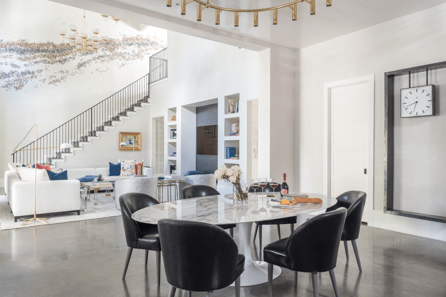 Black chairs surround a marble top dining table in an open concept living area, designed by Laura U.