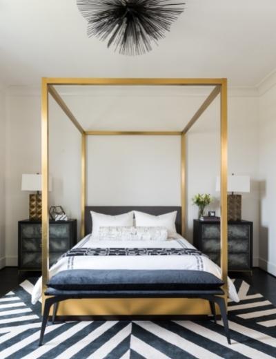 Geometric black and white rug rests below a gold canopy bed with a spiked light fixture hanging overhead