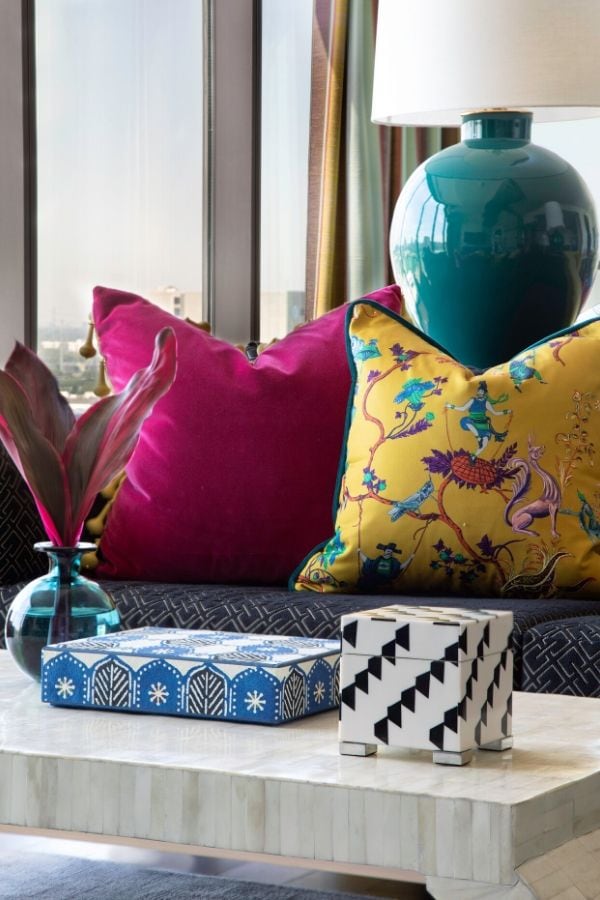 A living room vignette with a teal hued lamp and chinoiserie pillows.