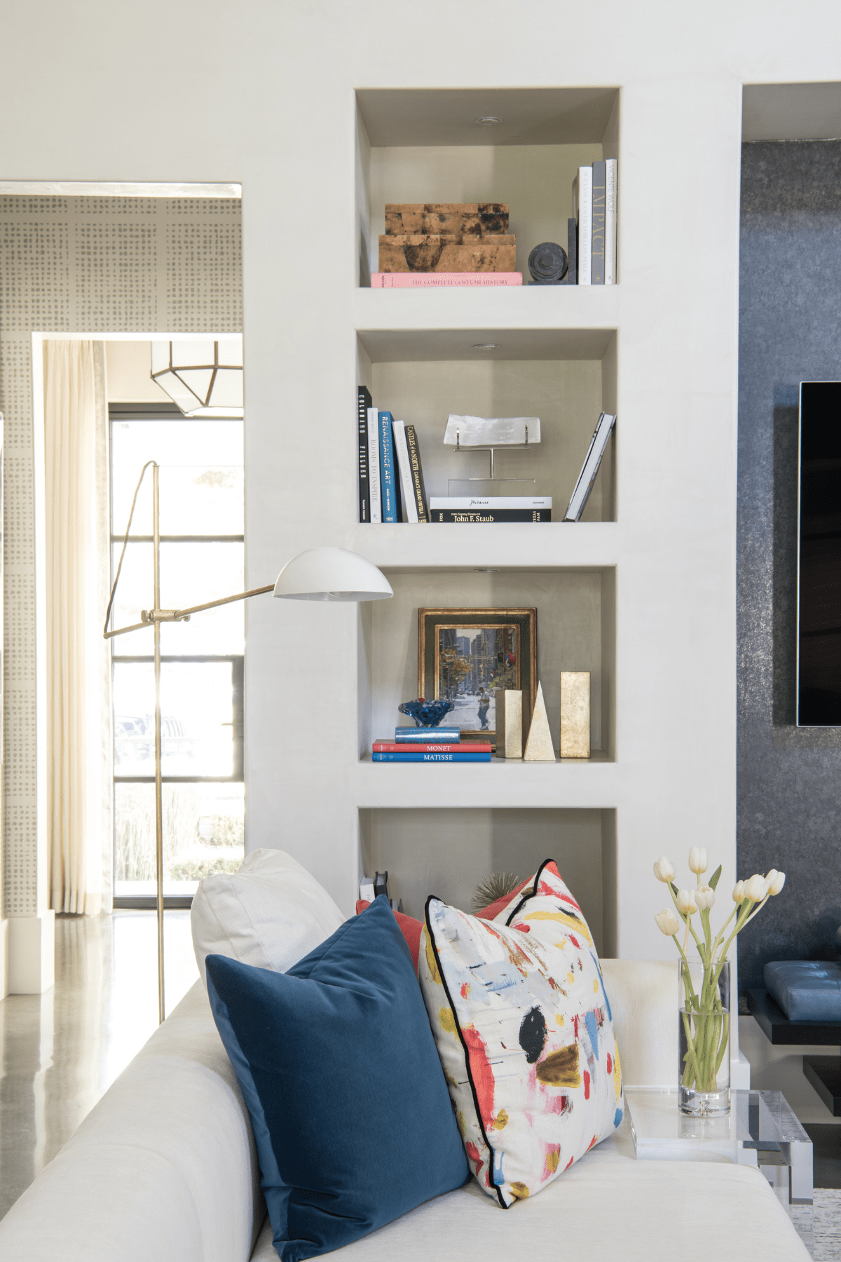 A floor lamp and sofa with vibrant, decorative pillows in front of a recessed shelf space.