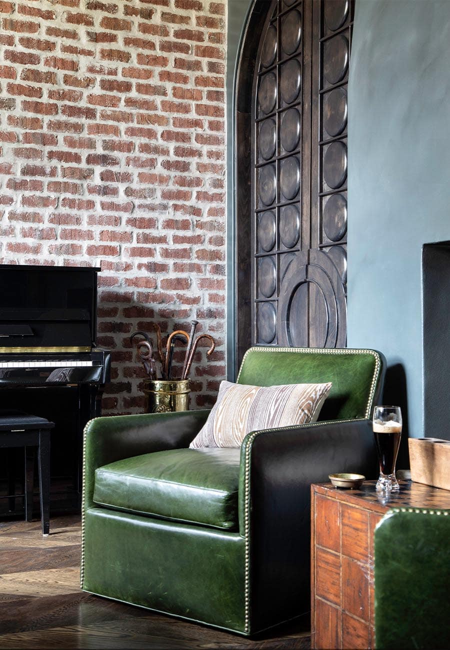 Green, leather club chairs positioned against an exposed brick wall in the home pub
