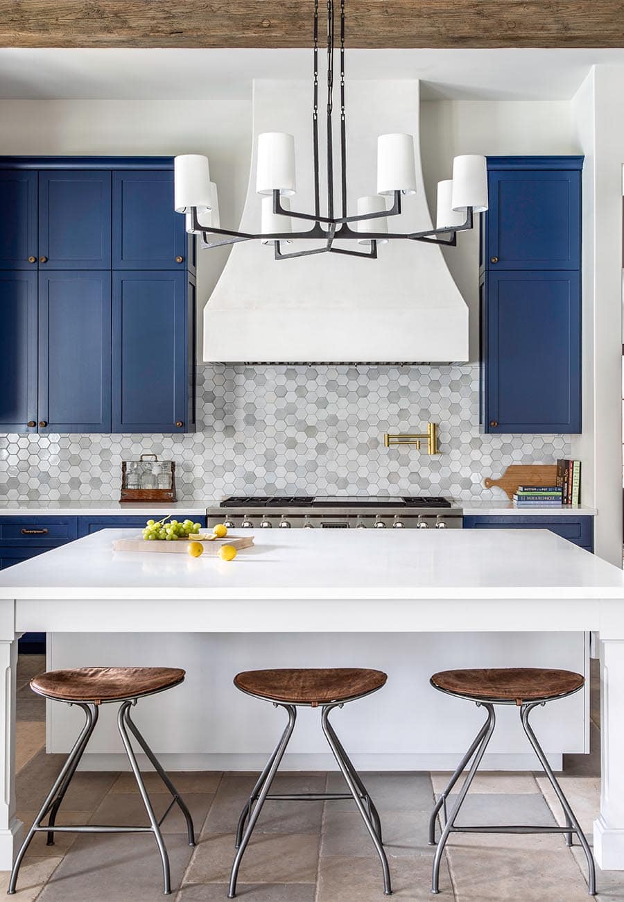 A bold kitchen with blue cabinets and white counter tops that complement wood beams and bar stools