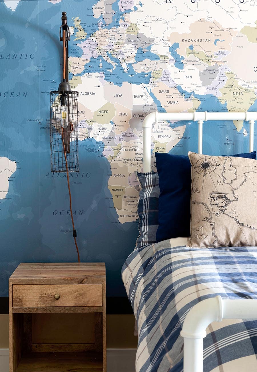 A map-themed boy's room with map wallpaper and a blue, plaid comforter