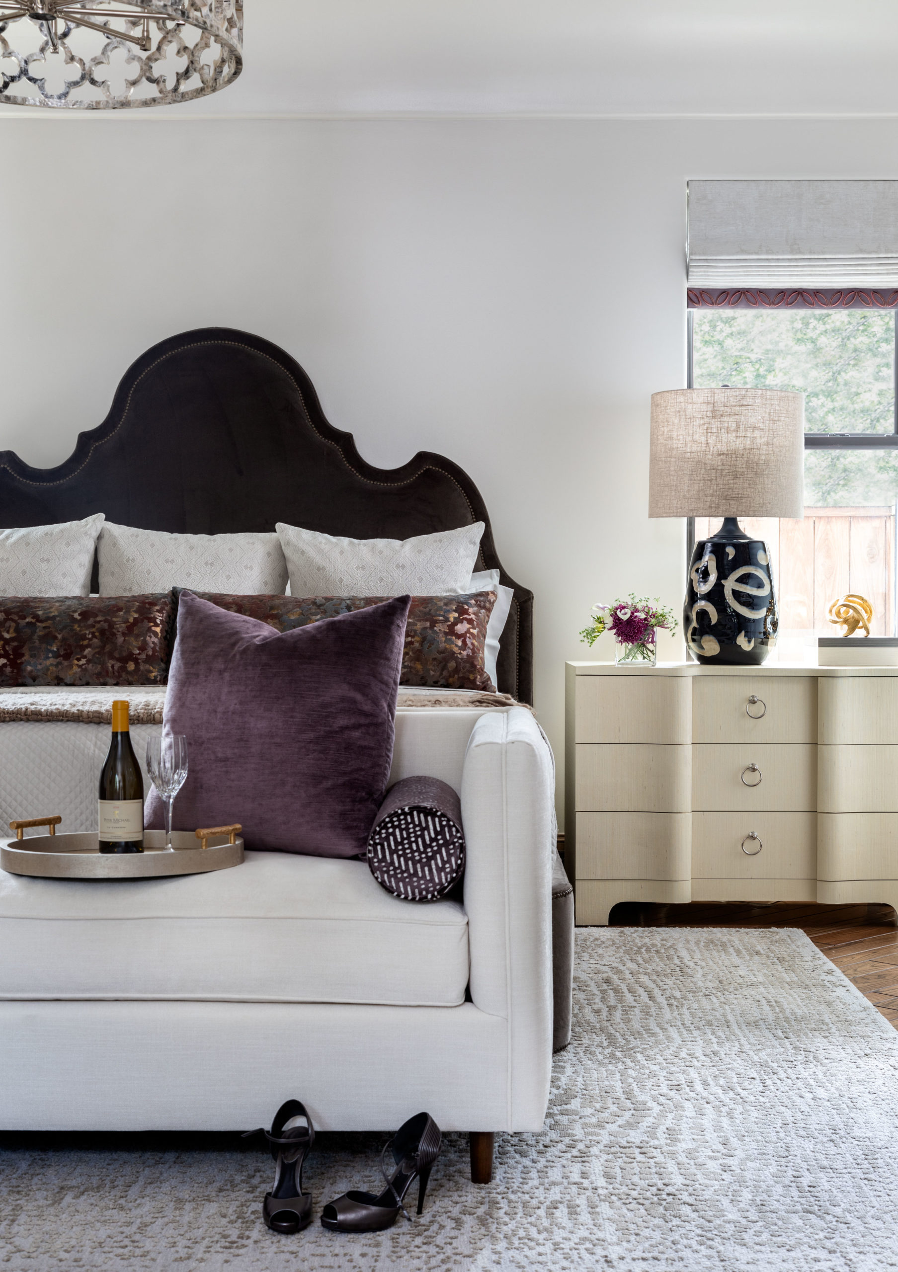 A Master bedroom with curved headboard and soft bench with lamp and nightstand