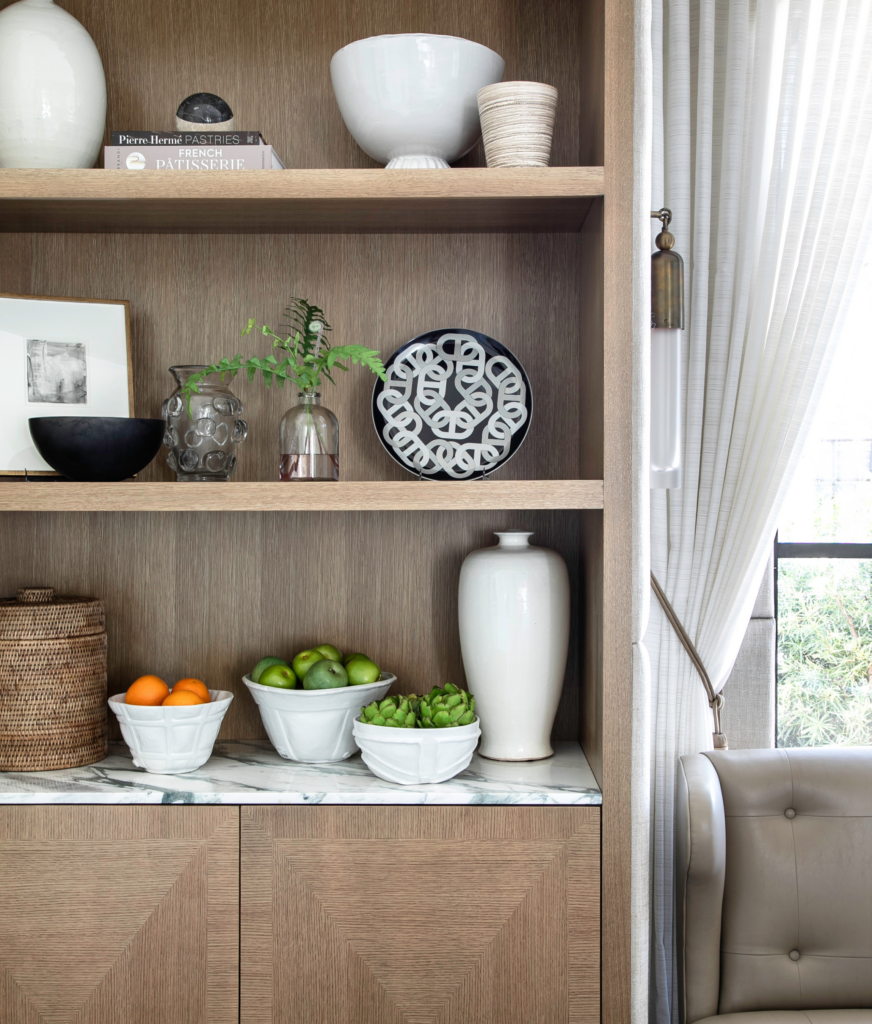 A vignette of a kitchen with handsome wood built-in shelves and stylish Sahco tiebacks