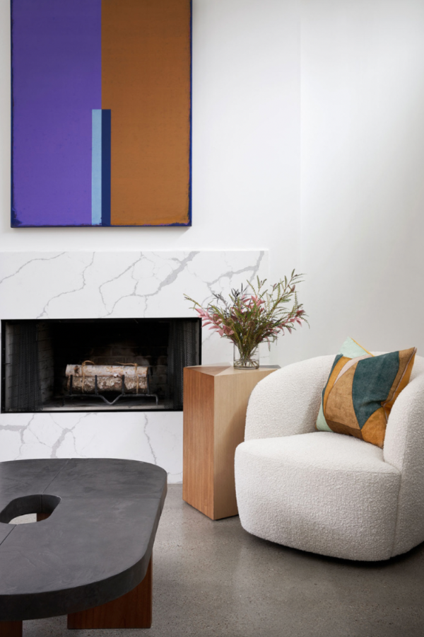 marble fireplace surround with abstract colorfield painting above and plush club chair to the right side