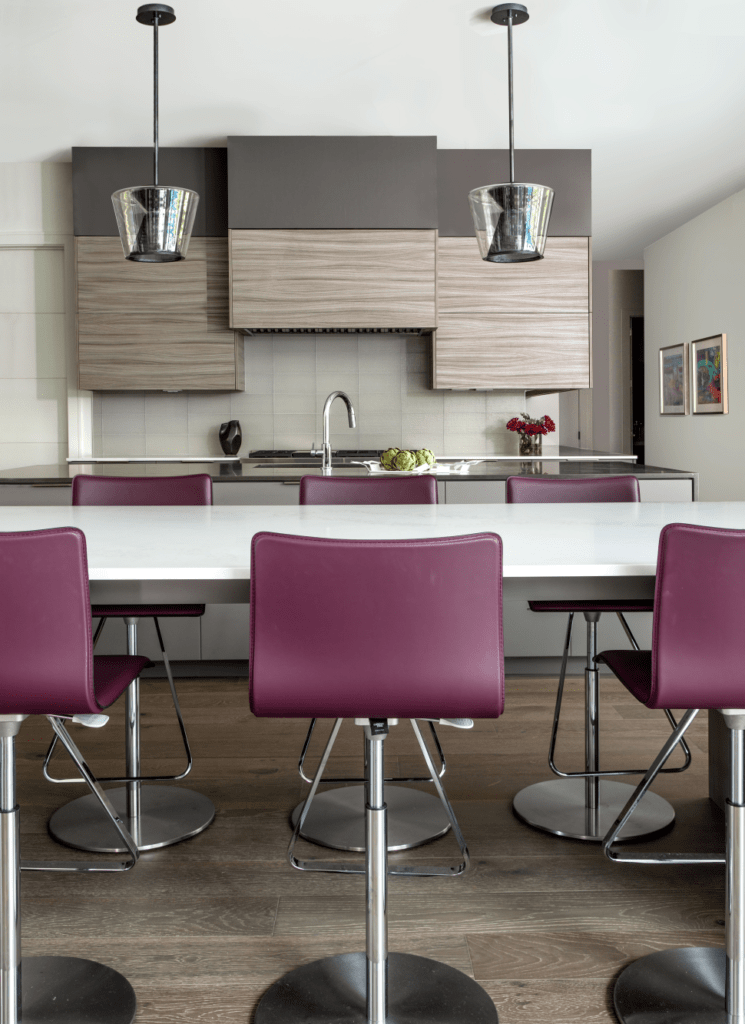 This modern kitchen is all about purple barstool, white countertop, brown cabinets & black pendant lights